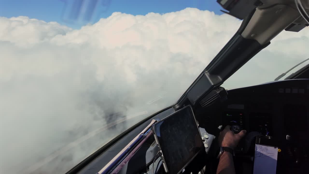 Hand of a caucasian pilot grasping the flight controls of a jet airplane while flying above cottony clouds, unfocused backgroud.