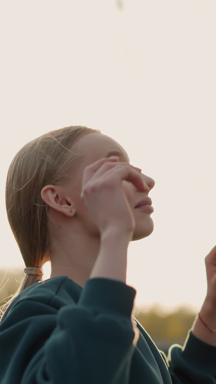 초록색 스웨터를 입은 여성이 야외에서 배구 경기를 하고 있으며, 그녀의 자세를 조정하여 전면에 명확한 배구 네트워크와 초록색과 건물의 배경으로 봉사합니다.