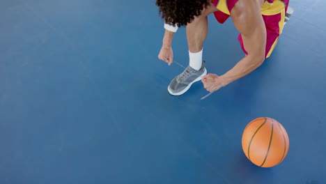 young biracial man ties his shoelaces on a basketball court