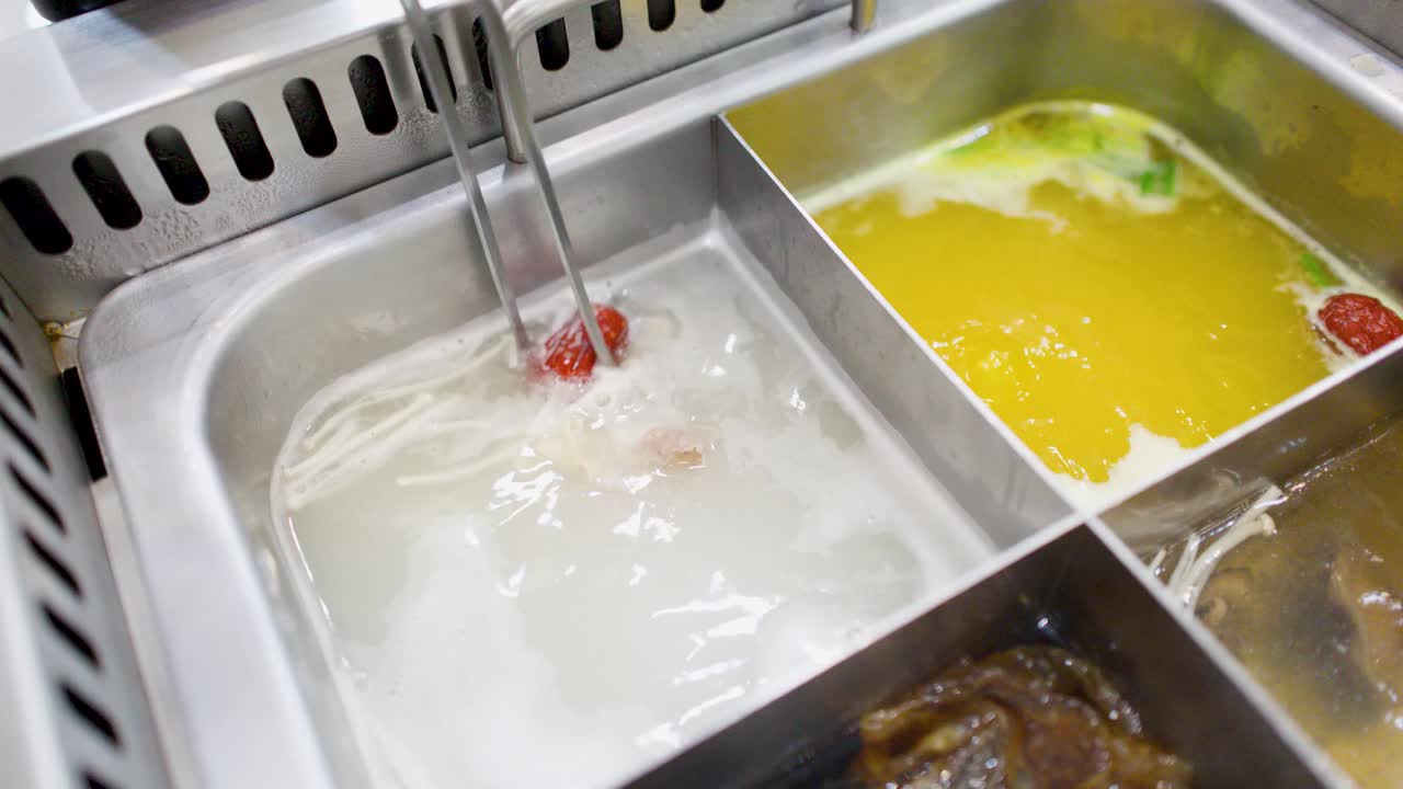Primo piano di bacchette che cuociono carne in una pentola bollente divisa con vari brodi.