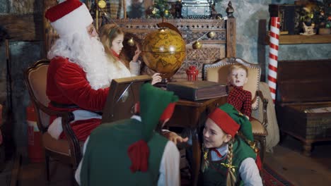 happy elves, santa claus and children having merry time. christmas atmosphere in santa's residence with fairy heroes and santa.