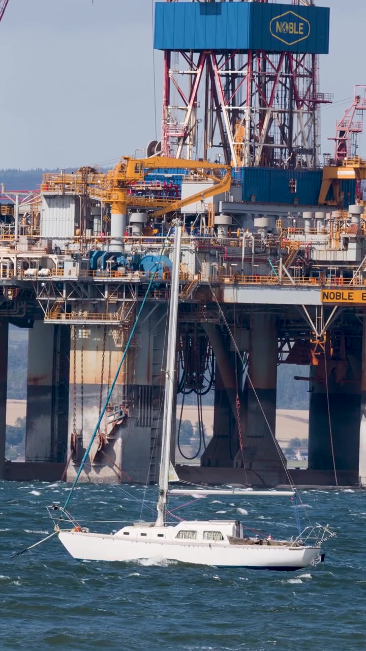 En hvid yacht sejler forbi en stor offshore olieplatform, industriel maritim scene, i dagslys, stabilt kamera