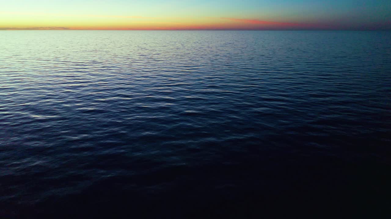 Calm ocean surface extends to the horizon at dusk with soft wave patterns and a warm gradient sky, creating a serene and tranquil seascape atmosphere