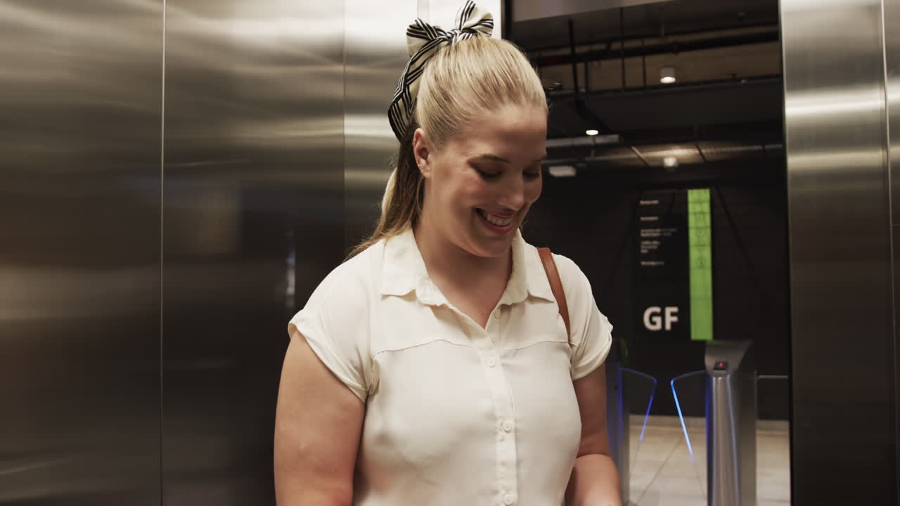 Using smartphone, woman smiling while standing in elevator, wearing white blouse