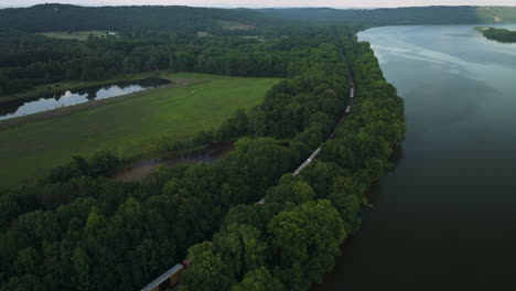 aerial flying above moving train passing next to arkansas river in spadra park