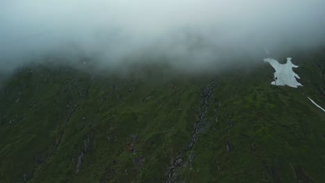 montañas verdes con cabinas de teleférico rojas entrando y saliendo de las nubes