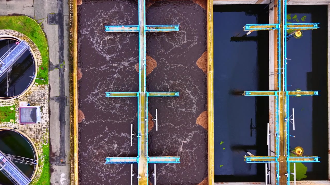 Vista dall'alto delle vasche di aerazione in un impianto di trattamento delle acque reflue. Angolazione a volo d'uccello che mostra acqua marrone schiumosa accanto a una vasca di decantazione limpida con passerelle blu