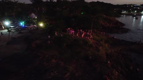 Gente-Viendo-La-Puesta-De-Sol-En-El-Bar-De-La-Playa-Junto-Al-Mar-Con-Luces-De-Colores-Disparadas-Con-Drones