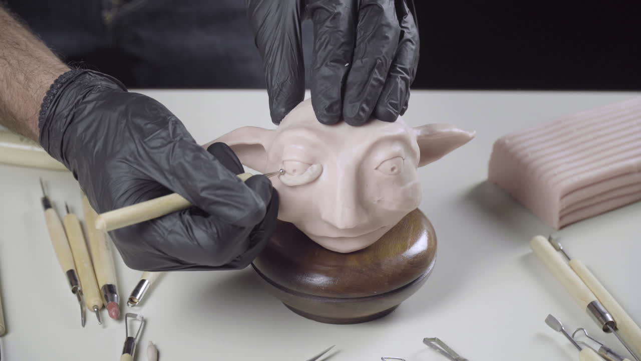 아티스트는 바늘 도구 4k를 사용하여 플라스틱 인형 머리의 눈을 모델로 만듭니다.