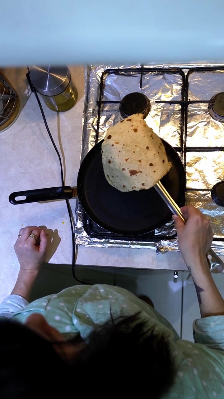 Ragazza che cucina il tradizionale pane chapati indiano in una padella di ghisa nera su un fornello a gas, girando e dorando l'impasto.