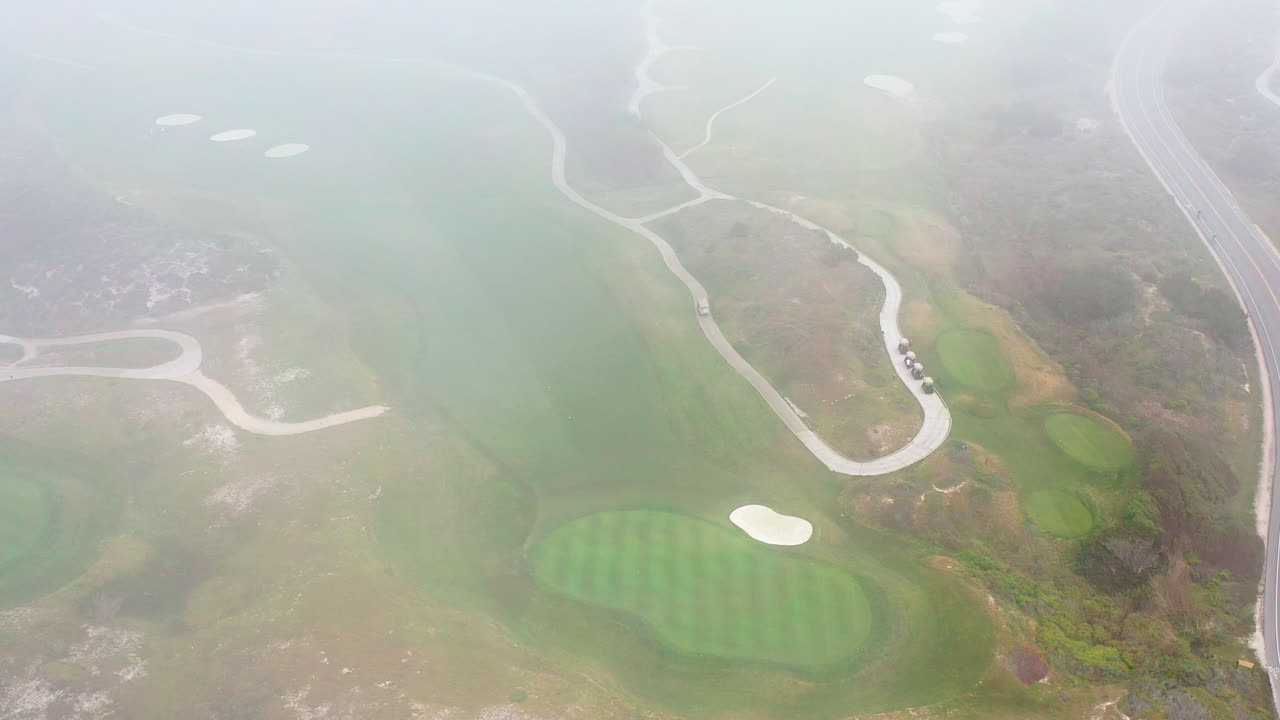 안개를 통해 드러난 골프 코스의 시네마틱 조감도