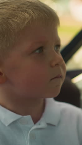 serious little boy in white polo shirt sits in motorboat cabin closeup. toddler child feels nervous while rides watercraft at resort. emotional kid