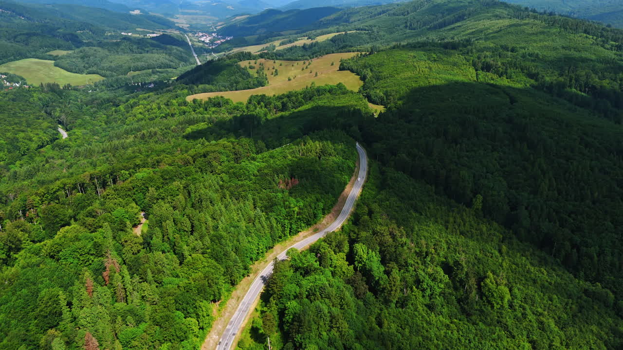 Winding road through green hills. A winding road cuts through dense forests and rolling hills under a clear blue sky, showcasing nature beauty