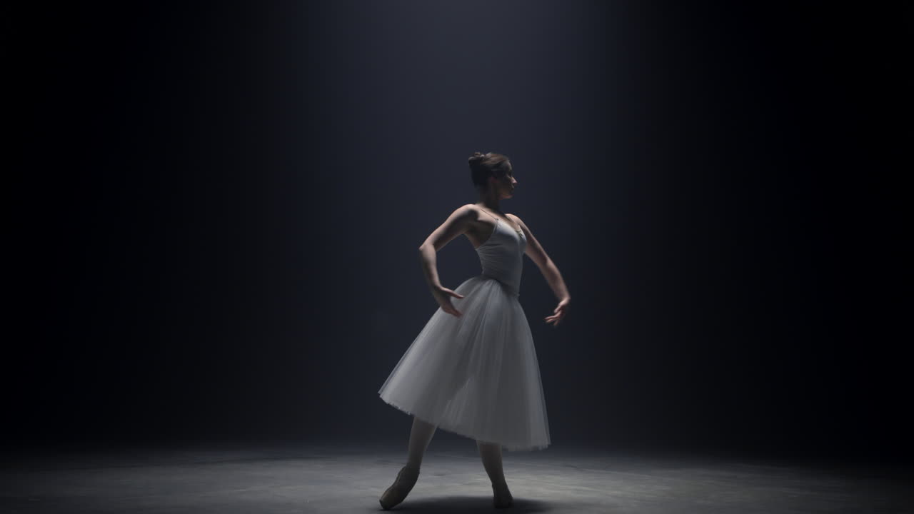 스포트라이트 아래 서 있는 유연한 발레리나. 발레 댄서가 무대에서 손을 움직인다.