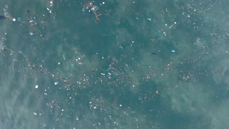 drone descendiendo de arriba hacia abajo disparado sobre agua contaminada llena de basura plástica en el agua tropical turquesa de la playa de balangan uluwatu bali indonesia