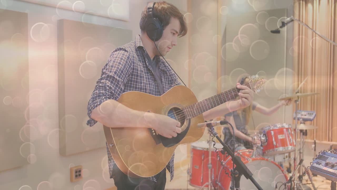 guitarist strumming acoustic guitar in music studio, drummer playing red kit light circles floating