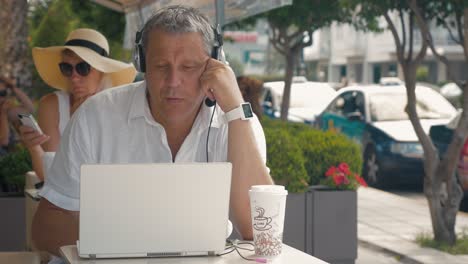 Hombre-Vestido-Con-Auriculares-Video-Chat-En-Una-Cafetería-Al-Aire-Libre