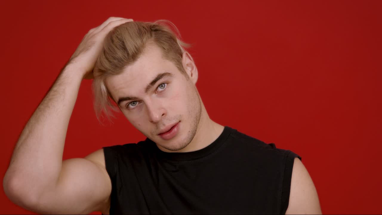 Giovane uomo con capelli biondi in camicia nera su sfondo rosso