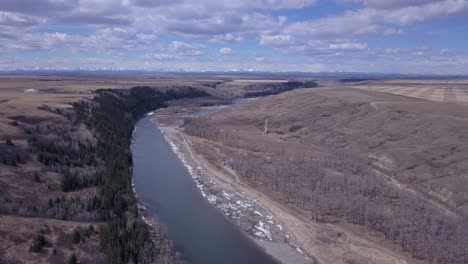 a prairie river valley in spring with mountain horizon and clouds