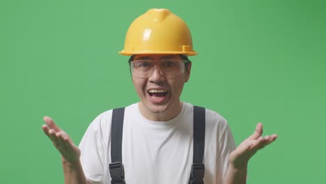 close up of wondering asian man worker wearing goggles and safety helmet saying why and standing doubtfully in the green screen background studio