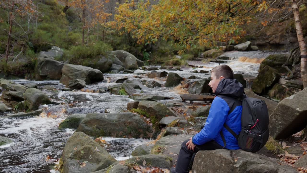 어린 소년이 앉아서 휴식을 취하고, 그의  ⁇ 기 부츠를  ⁇ 고, 가을 야외 풍경 장면에서