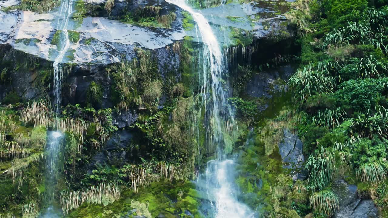 plano general de la cascada que fluye cuesta abajo montañas con vegetación - milford track en nueva zelanda