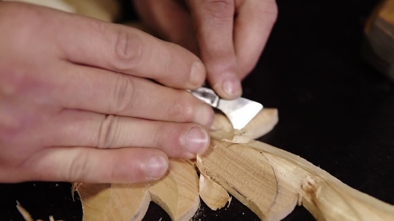 Close up footage of man's hands, he is curving a small details on the piece wodden pattern - floral ornament in work shop on the work table using small planer