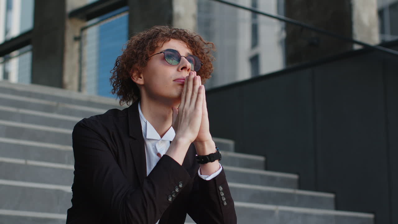 Nervous businessman manager with hands joined making company decision pray sitting on office steps