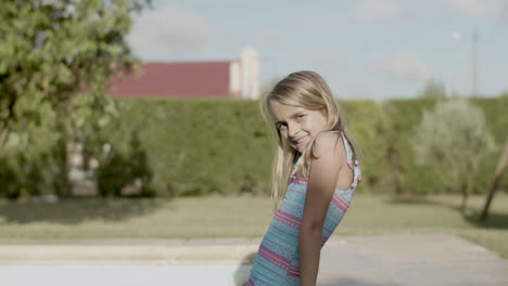 young girl sitting on poolside, smiling and squinting from sun.