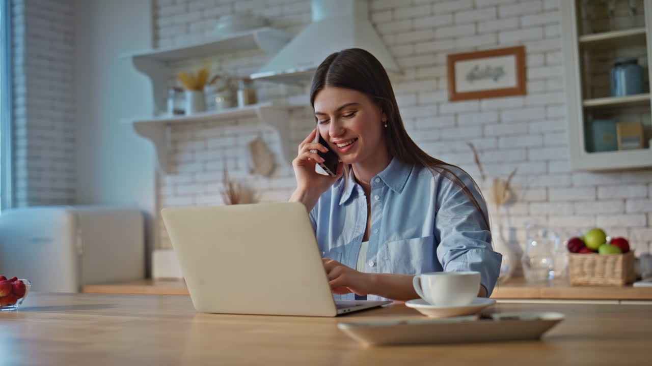 Happy housewife talking smartphone at home kitchen closeup. Lady using laptop
