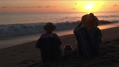 a couple toasts the ocean from their beach chairs