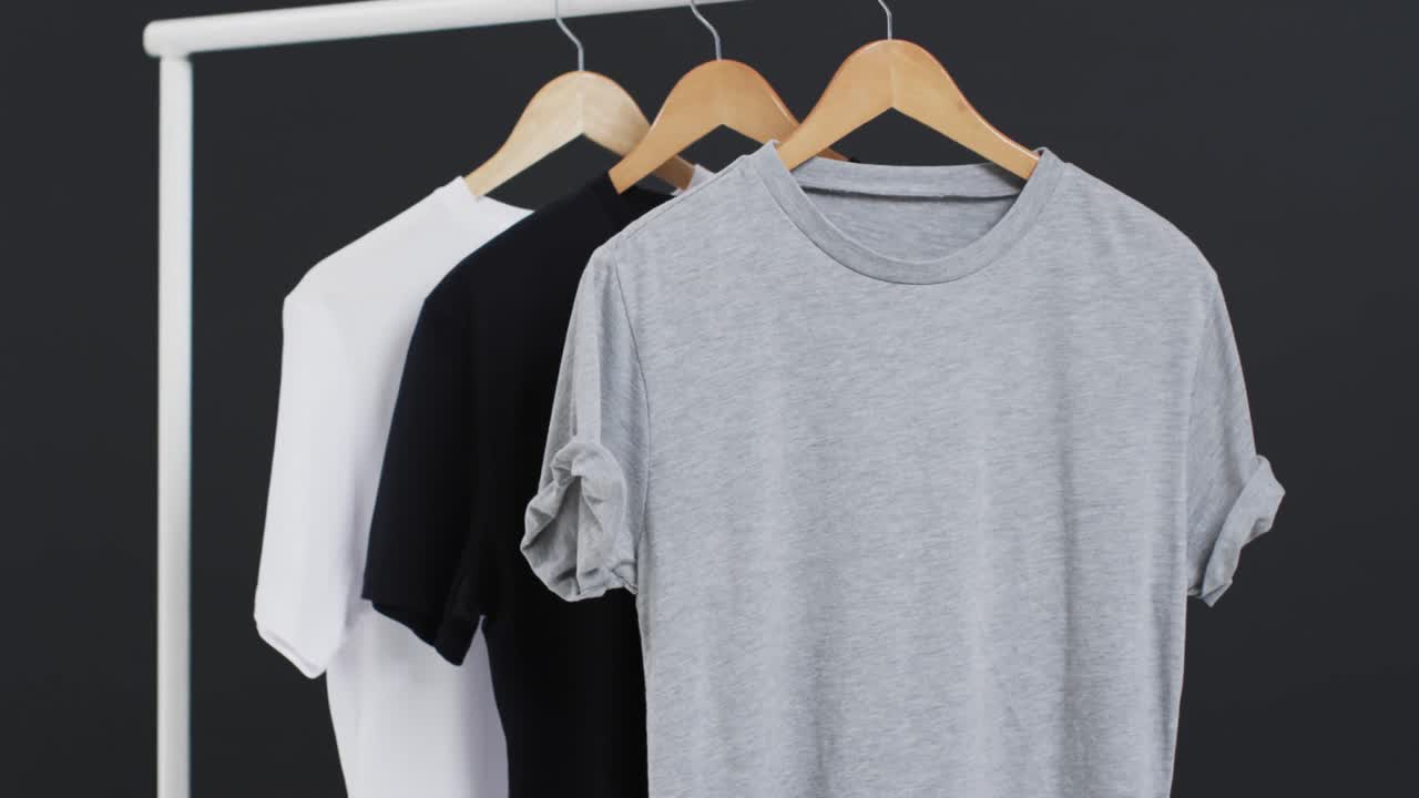 Video of three white, black and grey t shirts on hangers and copy space on black background
