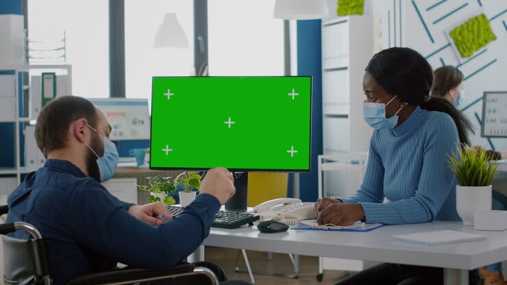 Manager in sedia a rotelle con mascherina che guarda un desktop con mockup.