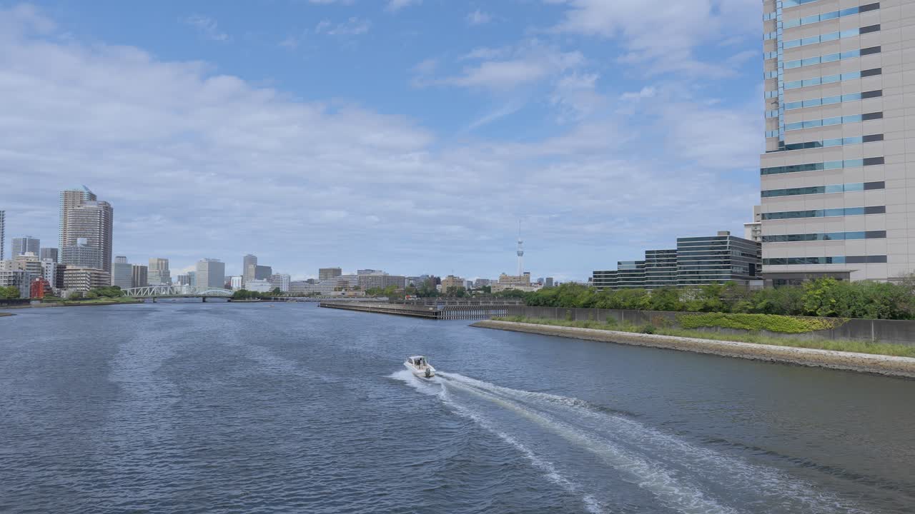 A peaceful shot of a passenger boat traveling down a river with the Tokyo cityscape and modern buildings in the background