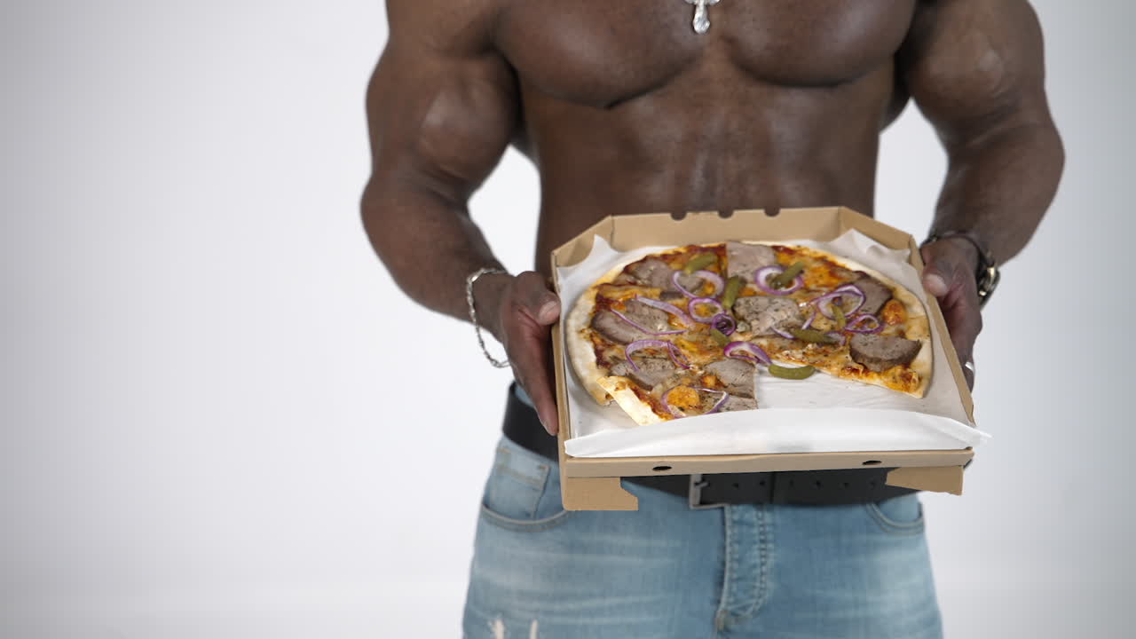 Tasty pizza in hands of african man. Black skinned guy with muscular body proposing delivered pizza in carton on studio background.