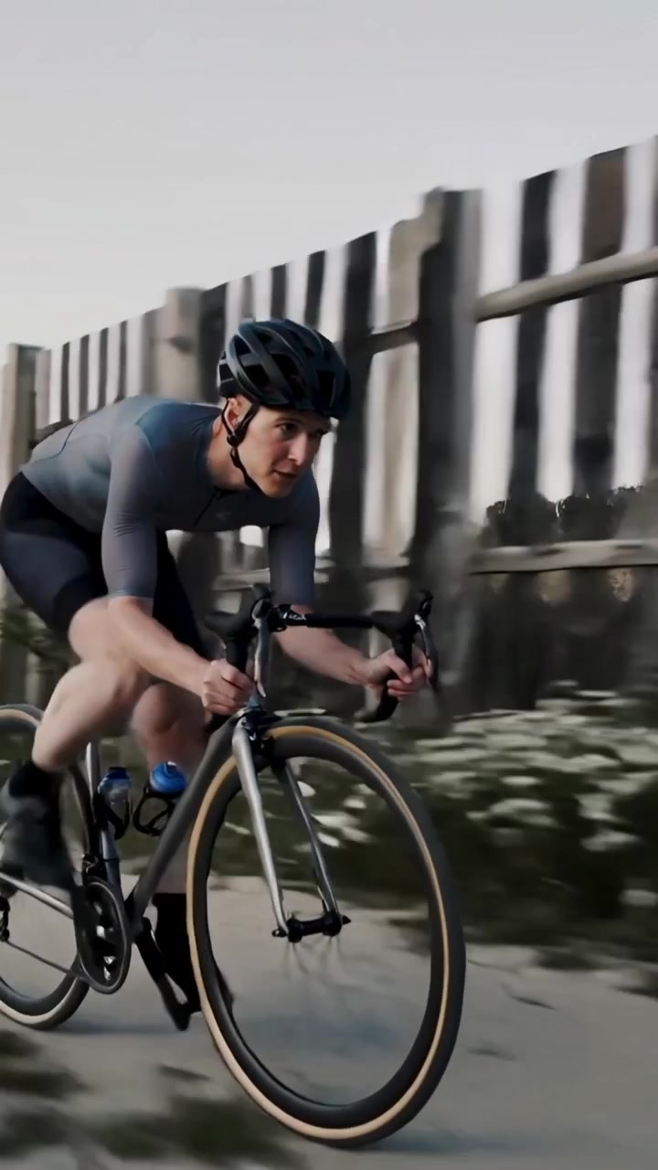 Video verticale: Ciclista che pedala in tenuta su bici da strada, mantenendo una posizione aerodinamica per la velocità su un sentiero oltre una recinzione