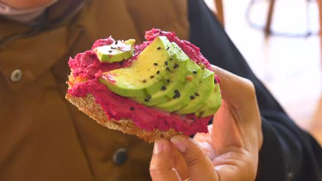 close-up of a hand holding avocado and beetroot hummus toast