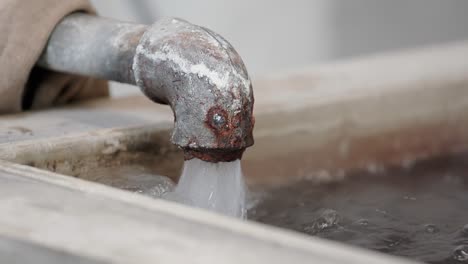 water flows out of a rusty pipe into a water tank in slow-motion