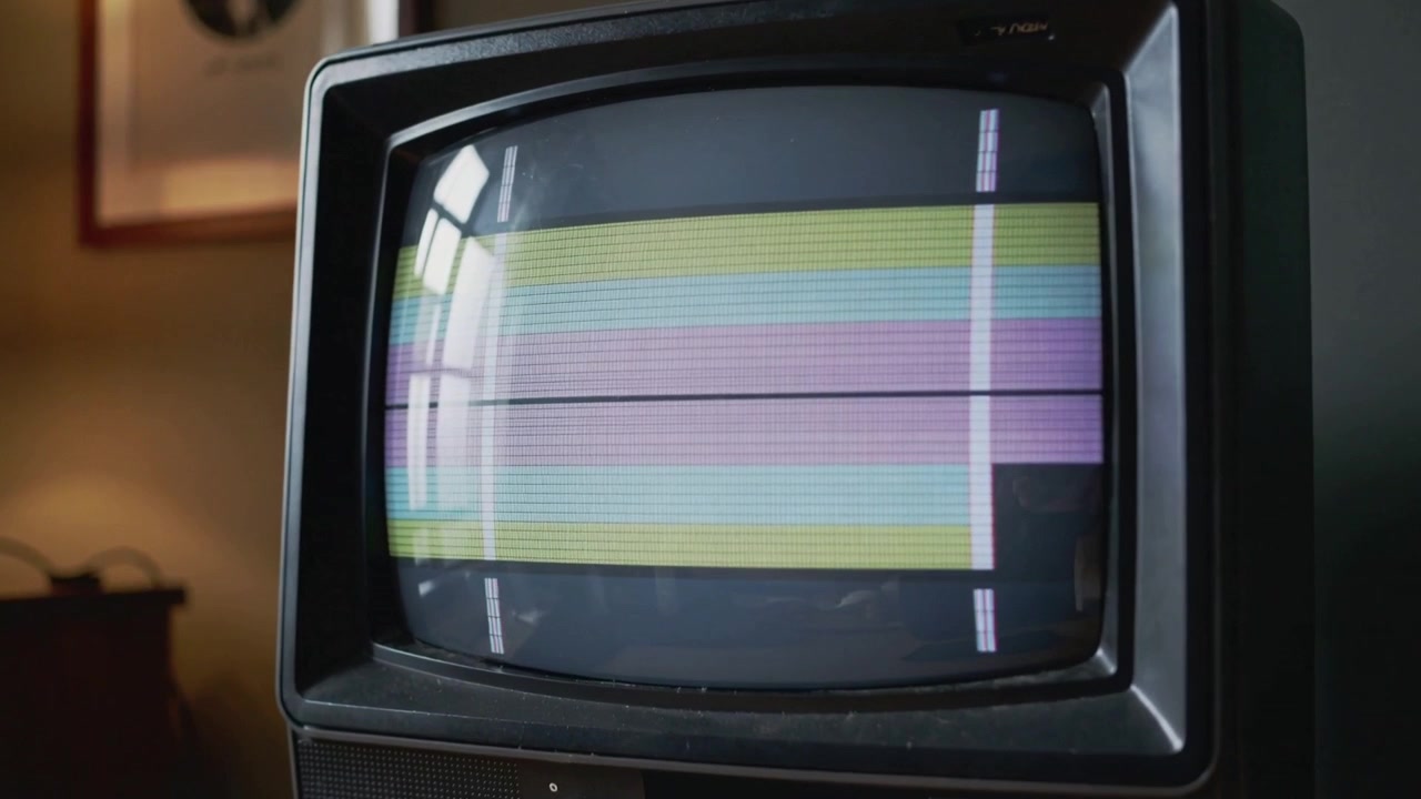 La telecamera si avvicina a un televisore CRT vintage su un tavolo di legno, mostrando linee di scansione e il riflesso di una finestra.