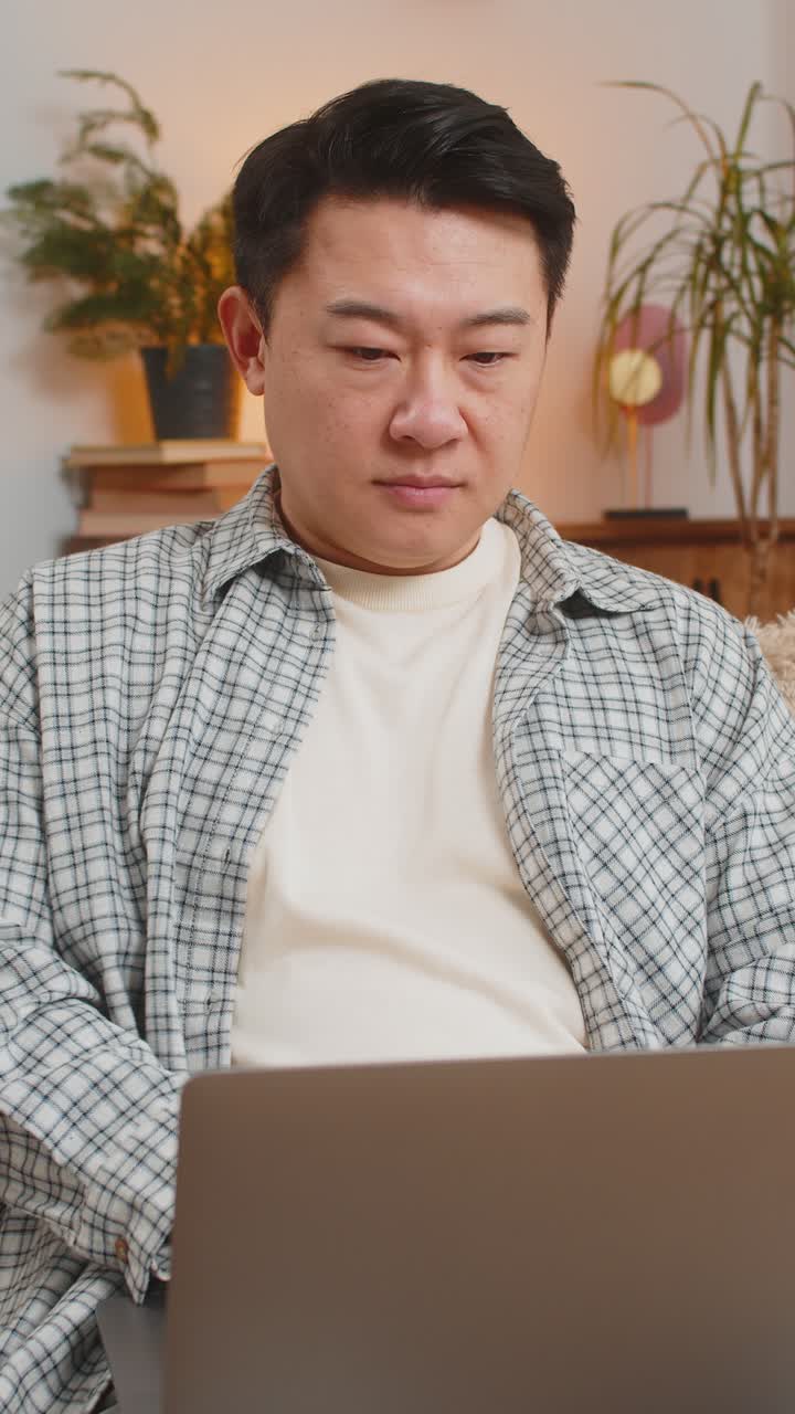 Happy mature chinese man sitting on couch closing laptop after finishing work in living room at home