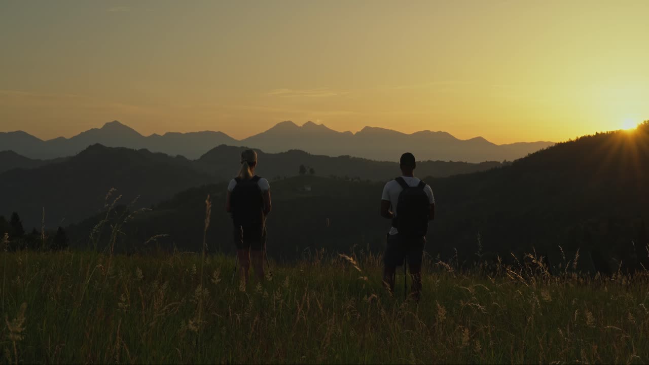Couple hikes at sunrise, pausing to enjoy the view of St. Thomas Church, Slovenia