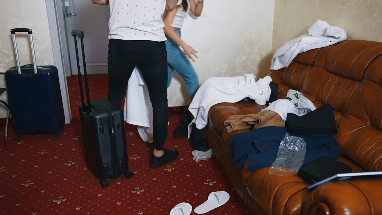 Young couple in a hotel room. Man and woman packing clothing after the holiday trip.Two suitcases for a trip. Clothes on sofa. Tourist couple adventure lifestyle.
