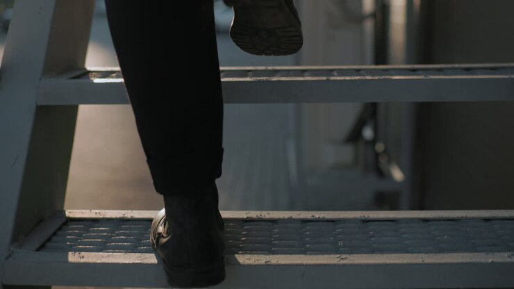 Back leg view man black shoe and trouser climbing staircase carefully with warm soft light reflecting off interlocked stone path, slow deliberate step, focus on movement