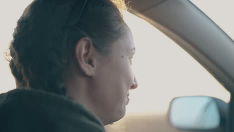 Una-Mujer-De-Pelo-Oscuro-Habla-Conduciendo-Un-Coche-A-La-Brillante-Luz-Del-Atardecer