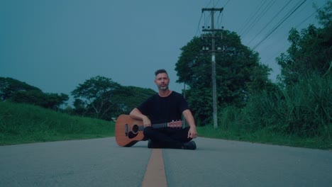 man playing acoustic guitar on a country road at dusk