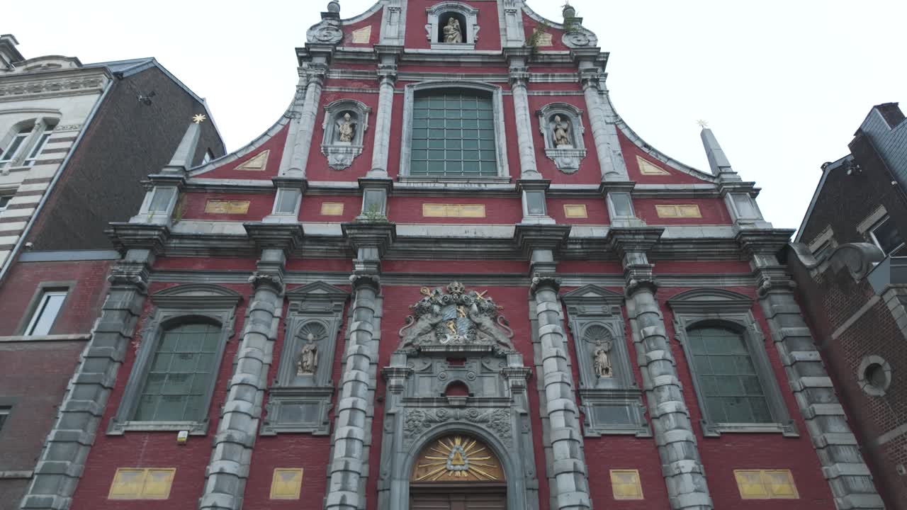 una fachada de iglesia barroca roja con estatuas, arquitectura dramática en lieja, bélgica