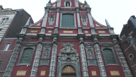 a red baroque church facade with statues, dramatic architecture in liège, belgium