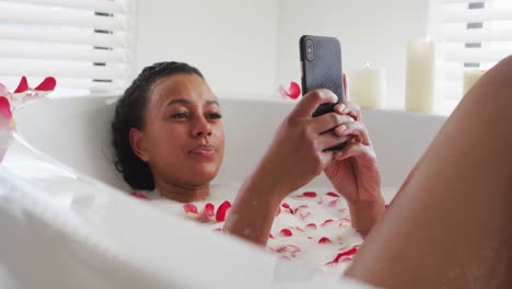 african american woman using smartphone in the bath tub in the bathroom at home