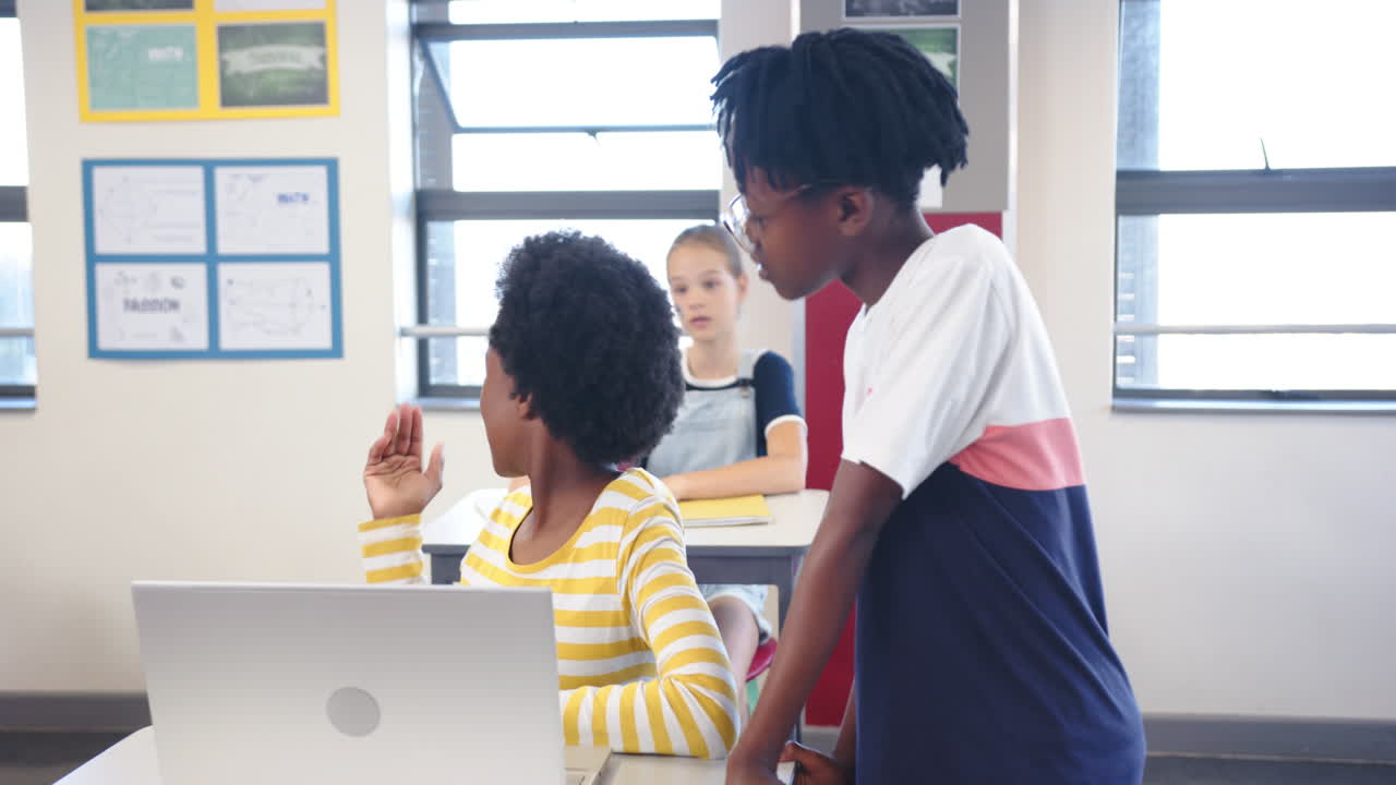 A scuola, due studentesse collaborano al portatile mentre un'altra studentessa passa.