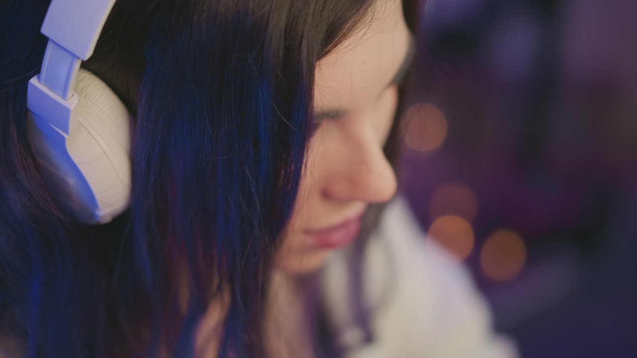close up profile of young woman with long dark hair wearing white headset focused intently downward with soft blurred background and dim purple lighting adding calm studio ambiance